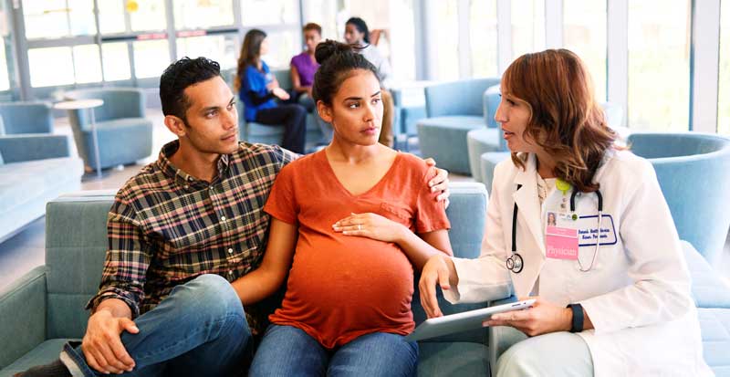 A pregnant woman and partner with her doctor in a health care setting.