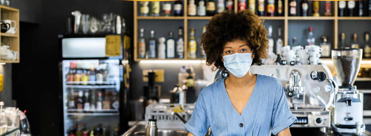 A woman working at a coffee shop wearing a mask.